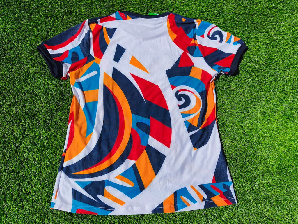 A short-sleeve crewneck t-shirt with a vibrant abstract geometric print, laid flat on a green grass background.