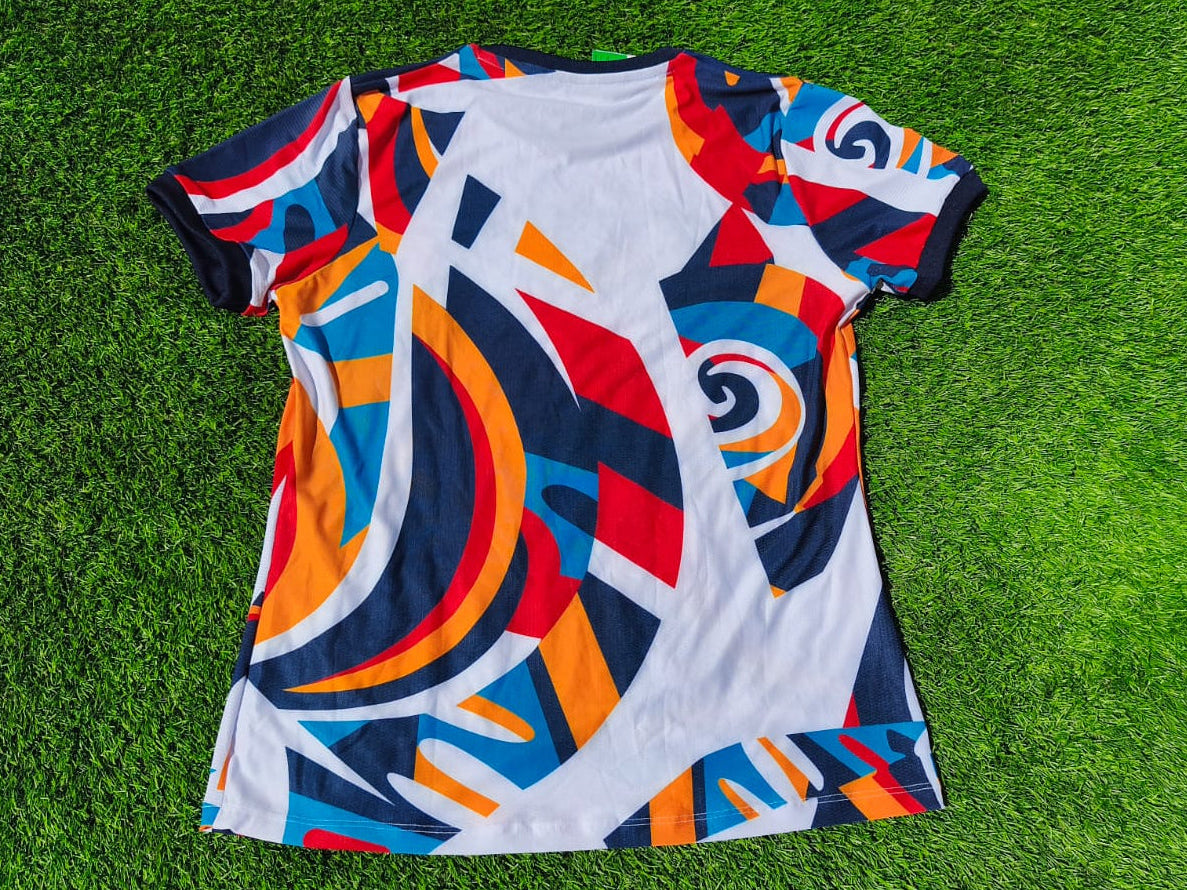 A short-sleeve crewneck t-shirt with a vibrant abstract geometric print, laid flat on a green grass background.